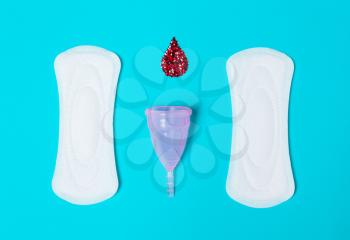 Pad, menstrual cup, with a drop of blood on a blue background. The view is flat. Concept of critical days, menstruation