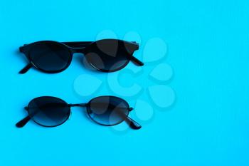 Two pairs of stylish black hipster sunglasses on a blue background