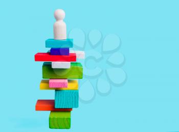 Concept of leadership, winner, creativity. Human figure on a pedestal on colored blocks on a blue background.