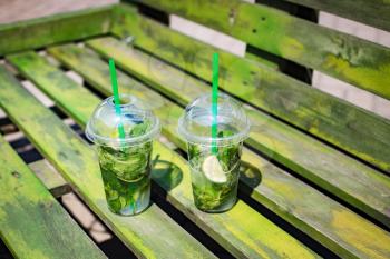 Mojito non-alcoholic in plastic glasses on a wooden green background, summer street festival