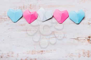 Origami paper hearts in transgender flag colors on wooden background