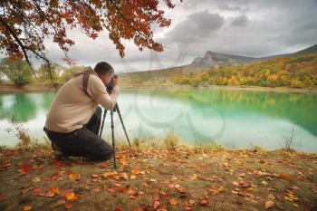 Professional photographer using a tripod takes a shot on the autumn lakes. Nature and people landscape.