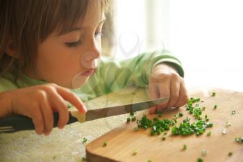 Daughter cutting green onion with knife. Food preparing and cooking scene.