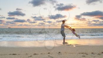 Father and daughter playing together on the sea beach at sunset. Emotional scene.