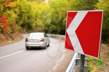 Car on autumn road and red turn sign. Nature and travel scene.