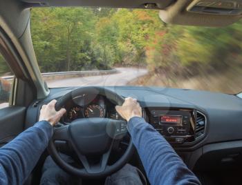 Man driver hands holding the car steering wheel. Fast speed and road in forest.