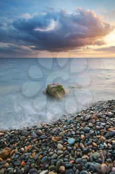 Sunset on the sea shore. Lightning stroke in cloudy sky. Stones and rainy cloud. Nature landscape composition. 