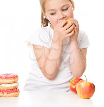 Cute little girl choosing between apples and cake, isolated over white