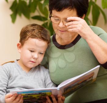 Grandmother is reading book with her grandson, indoors