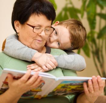 Grandmother is reading book with her grandson, indoors
