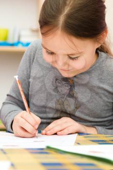 Cute girl is drawing using color pencils while sitting at table