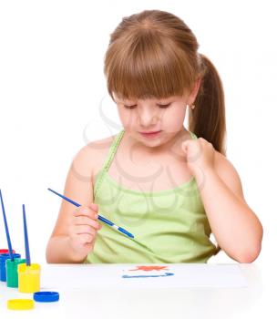 Cute thoughtful child play with paints while sitting at table, isolated over white