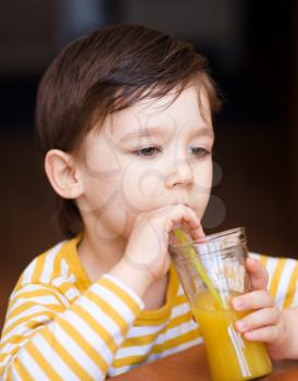 Little boy is drinking orange juice using straw