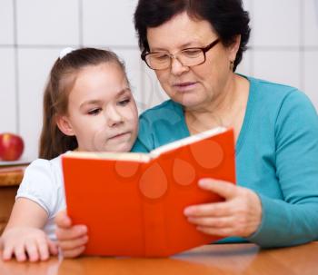 Grandmother is reading book with her granddaughter, indoors