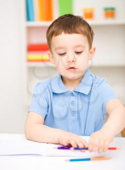 Little boy is drawing on white paper using color pencils