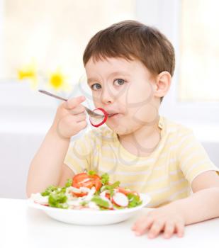 Cute little boy eats vegetable salad using fork