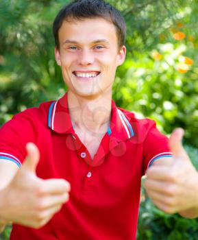 Young happy student is showing thumb up sign using both hands