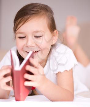 Cute little girl is reading book while sitting on a couch, indoor shoot