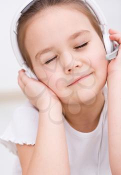 Cute little girl is enjoying music using headphones and closed her eyes