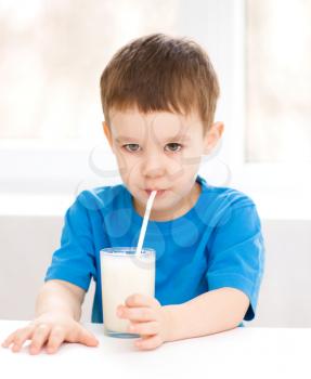 Cute little boy is dipping his tongue in the glass of milk