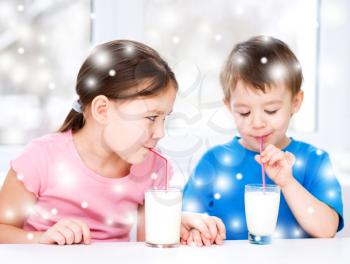 Cute little girl and boy drink tasty fresh milk, over snowy background