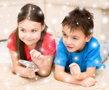 Happy girl and boy watching tv, remote control, over snowy background