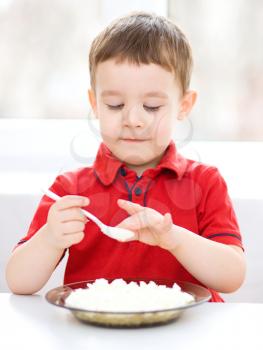 Cute little boy is eating cottage cheese using spoon