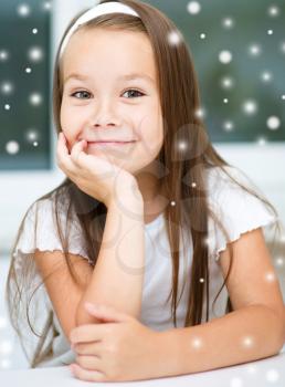 Cute girl is daydreaming while sitting at table, over snowy background