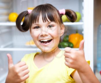 Happy girl standing near refrigerator with fruits and vegetables