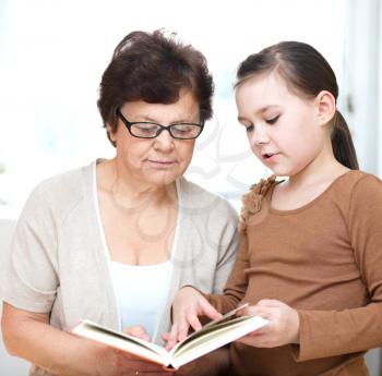 Cute grandmother is reading book with her granddaughter, in home