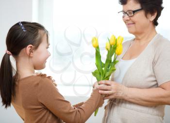 Happy grandmother with granddaughter. Woman and child with bouquet of flowers at home