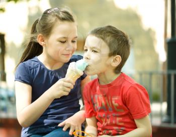 Girl is feeding his little brother with ice-cream. Outdoor