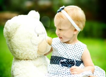 Little cute girl is playing her teddy bear, outdoors