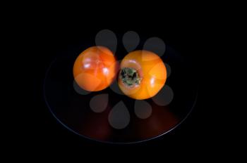 Ripe Golden two persimmons on plate and black background