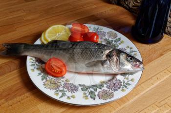Sea bass, spigola. Fresh fish with the head on plate. Kitchen table home cooking.