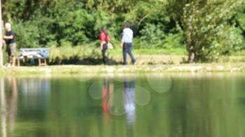 Shot of lake scenic in summer. Blurred nature unfocused background. Lake and forest. People with fishing rods.