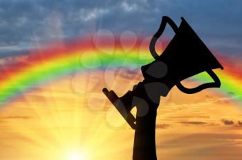 Winning the cup sport. Human hand holding the cup on the background of rainbow sunset