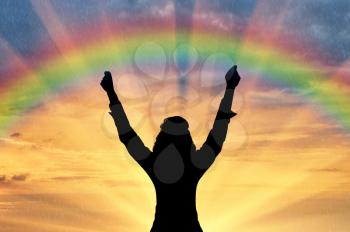 Emotion of happiness. Silhouette of a happy man with his hands up against the sunset and the rainbow