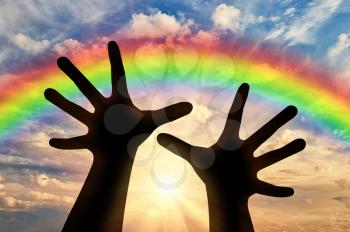Religion and prayer. Hands reach for sky at sunset and rainbow