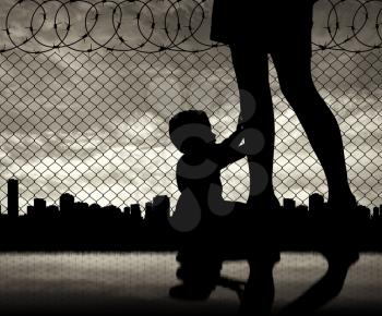 Refugee family concept. Silhouette of the child and refugee mothers legs near the border on the background of the urban landscape