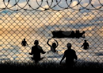 Refugees concept. Refugees swim to shore against the backdrop of barbed wire fence