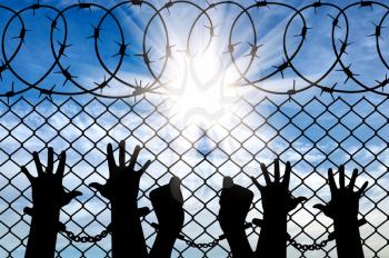 Silhouette of a crowd of hands in handcuffs near the fence with barbed wire