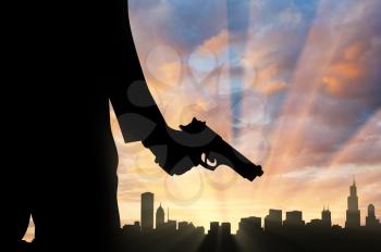 Terrorist concept. Pistol in hand terrorist, against the background of the urban landscape at sunset