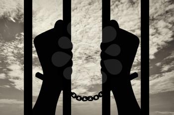 Freedom concept. Silhouette of human hands in handcuffs behind bars