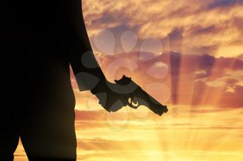 Terrorist concept. Pistol in hand terrorist on sunset background