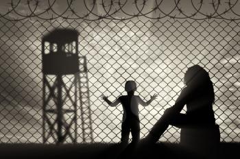 Refugees concept. Mother with a small child refugees, near the fence of barbed wire on the background of the watchtower