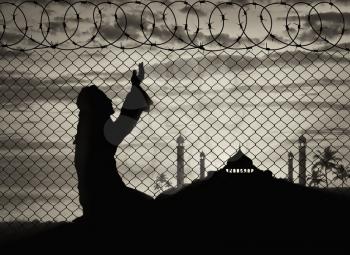 Islamic religion. Muslim Praying near the fence of barbed wire on the background of the mosque