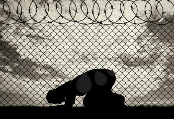 Religion Islam refugees. Muslim prays near the fence of barbed wire