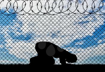 Religion Islam refugees. Muslim prays near the fence of barbed wire