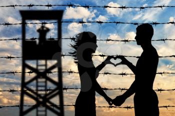 Refugees concept. Male and female refugees show hands symbol heart on the background of the fence and watchtower